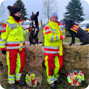 Zwei Frauen stehen vor einem Felsstein. Darauf sitzen erh&ouml;ht ihre beiden Hunden. Die Frauen tragen beide Einsatzkleidung. Dicke gelb rote Winterjacken mit Reflexionsstreifen.